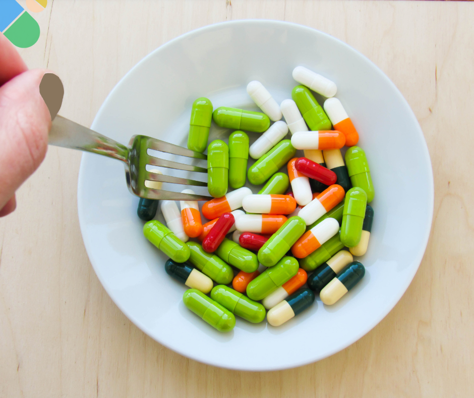 Colorful medication tablets and capsules on a fork against a white plate background