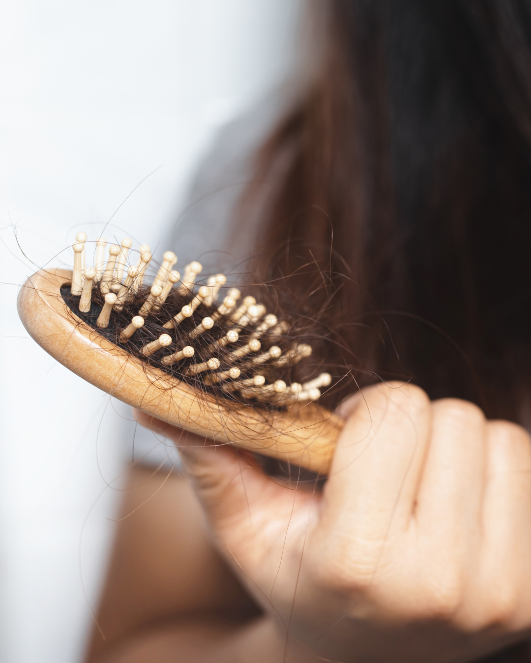 Woman holding a wooden hairbrush filled with shed strands of dark hair
